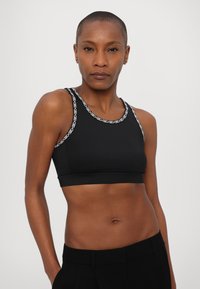 Black athletic crop top featuring a round neck, sporty design, and contrasting white chain pattern along the straps. Smooth texture.