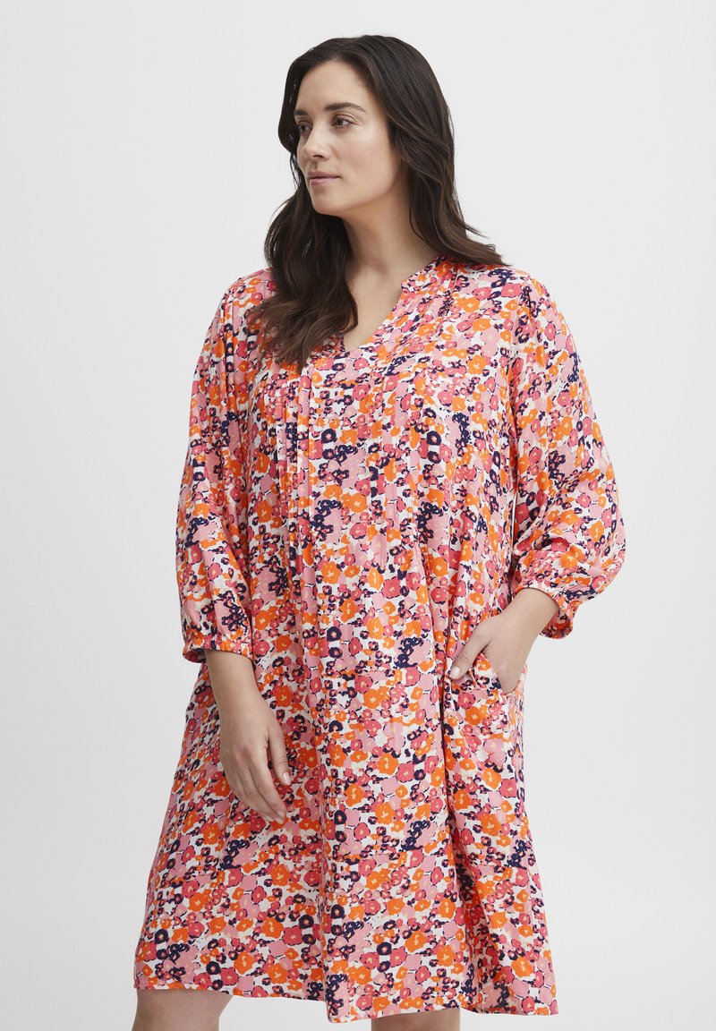 Rochie florală, până la genunchi, de culoare roz cu modele portocalii, purpurii și albe. Are decolteu în V, mâneci relaxate și buzunare laterale.