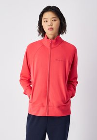 Rode zip-up jack met hoge kraag, raglanmouwen en zijzakken, gemaakt van zachte stof met geborduurde logodetails.