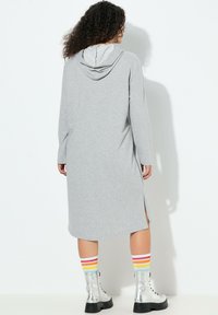 Harmaa hupullinen mekko, jossa pitkät hihat, sivuhalkiot ja rento istuvuus. Yhdistetty hopeisiin saappaisiin ja monivärisiin raitaisiin sukkiin.