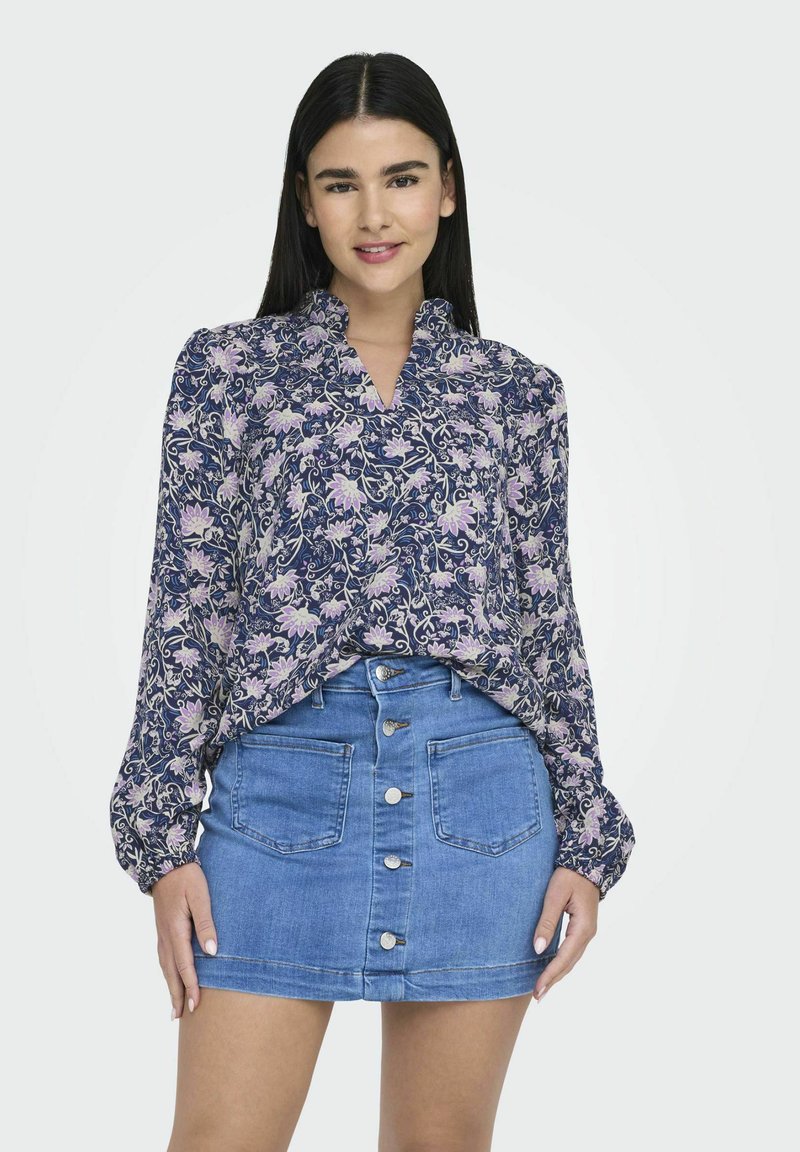 Blommig blus i marinblått med lila accenter och V-ringning, tillsammans med en ljusblå denimkjol med central knappstängning och fickor.