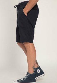 Tmavě modré bavlněné šortky s elastickým pasem, bočními kapsami a volným střihem. Nosené s vysokými tmavě modrými teniskami.