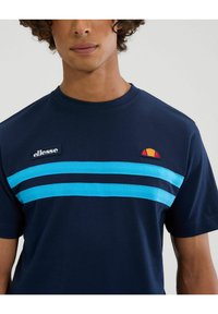Camiseta de algodón azul marino con dos franjas horizontales de color azul claro, parche de logo de la marca en el lado izquierdo del pecho y escote redondo.