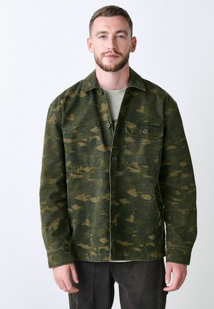 Green camo-patterned jacket, made of cotton, featuring a button-down front, two chest pockets, and a relaxed fit.
