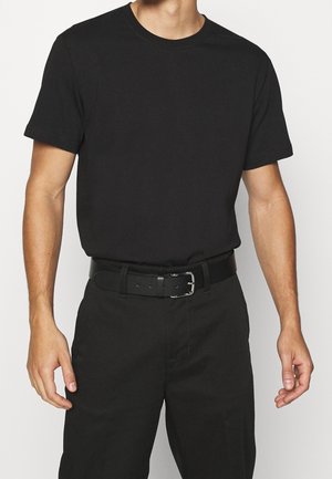 T-shirt en coton noir à manches courtes et col rond, associé à une ceinture noire avec boucle en métal argenté, porté avec un pantalon noir.