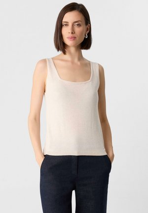 Beige mouwloze top met een vierkante halslijn, van lichtgewicht gebreide stof en met een geribbelde zoom, gecombineerd met donkere, op maat gemaakte broeken.
