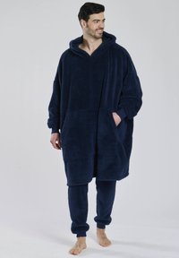 Marineblå fleece poncho med hætte, stor frontlomme og lange ærmer, parret med matchende fleecebukser. Blød tekstur og afslappet pasform.