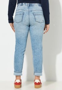 Jeans in denim azzurro chiaro con vestibilità comoda, vita elasticizzata, risvolti alle caviglie e due tasche posteriori. Le scarpe hanno un design rosso e bianco.