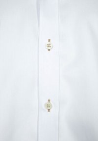 Camicia bianca con bottoni, realizzata in tessuto strutturato, con quattro bottoni rotondi color crema lungo la patta e cuciture a contrasto.