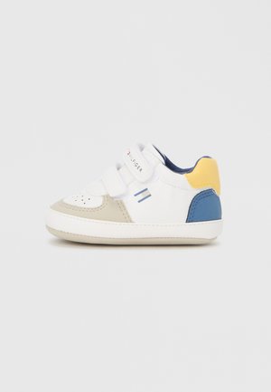 Baskets blanches avec des accents beiges, bleus et jaunes ; elles comportent deux bandes Velcro, un dessus perforé au niveau des orteils et une semelle en caoutchouc.