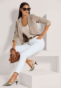 Beiger Wildleder-Blazer, cremefarbenes Tanktop, weiße Slim-Fit-Jeans, goldene und schwarze Schlangenleder-Slingback-Schuhe und eine kleine braune Handtasche.