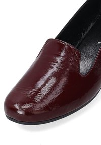 Burgundy patent leather slip-on shoe with a rounded toe and smooth surface. Features a low, black rubber sole and minimal stitching details.