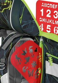 Mochila con una tela de patrón en verde oscuro y negro, que presenta una plantilla de stencil roja brillante y un tirador de cremallera en verde lima con un diseño de hoja.