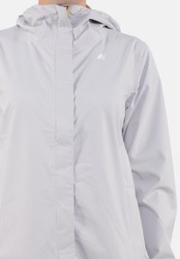 Giacca da pioggia grigio chiaro con cappuccio, dotata di zip frontale, con branding minimale e tessuto liscio e resistente all'acqua.