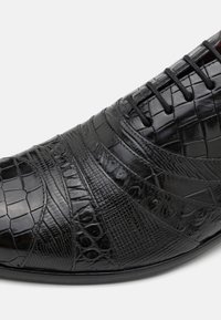 Scarpa in pelle nera caratterizzata da un design testurizzato con motivi rettiliani, chiusura con lacci e una finitura liscia e lucida.