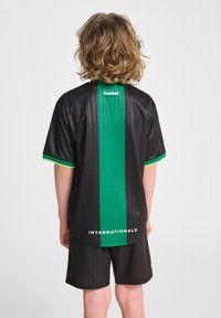 Svart sporttröja med gröna vertikala ränder, korta ärmar och texten "INTERNATIONALS" längst ner. Svarta shorts kompletterar outfiten.