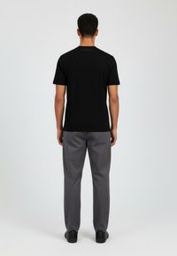 Musta lyhythihainen t-paita ja harmaat housut. T-paidassa on pieni logo takana. Sileä kangas, rento istuvuus ja suora leikkaus.