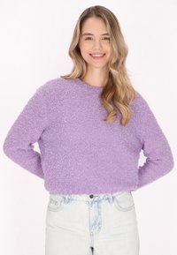 Pulover mov cu blană, cu decolteu rotund și mâneci lungi, combinat cu blugi de talie înaltă, de un albastru deschis. Textură moale, cu un croi scurt.