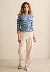 Blå och vitrandig långärmad skjorta i kombination med vida beige byxor. Byxorna har dragsko i midjan och en slät tygkvalitet.