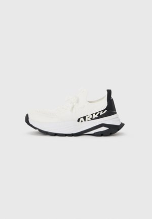 White athletic shoe with a textured knit upper, black accents, chunky sole, and a prominent black logo on the side.