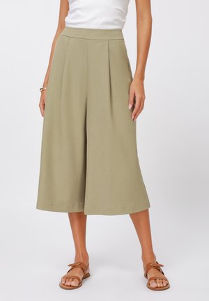 Licht olijfgroene geplooide culottes met een hoge taille, gecombineerd met bruine platte sandalen. Soepele textuur en op maat ontworpen.