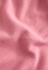 Tissu tricoté doux et rose avec une texture fine et uniforme, présentant de délicates plis créant des ombres et des reflets subtils.