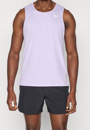 Mężczyzna ubrany w fioletowy sportowy tank top bez rękawów i czarne krótkie spodenki do biegania, stojący na jednolitym tle.