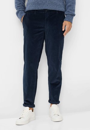 Marineblå corduroy bukser med slim fit, der har subtile lodrette ribber, sidelommer og oprullede manchetter, parret med hvide sneakers.