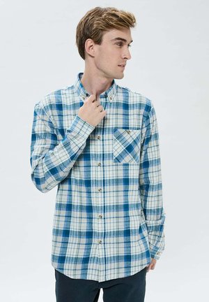 Chemise à manches longues à carreaux bleus et blancs avec un col boutonné, dotée d'une poche avant et de boutons marron. Texture douce en flanelle.