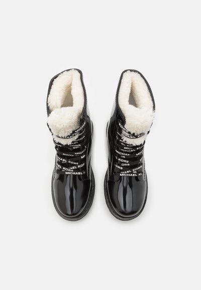 Bottes en cuir verni noir avec doublure en fausse fourrure blanche et lacets de marque contrastants noirs et blancs, présentant un design à lacets et un bout rond.
