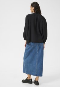 Black textured puff-sleeve top paired with a long blue denim skirt. The outfit features a relaxed fit and casual black shoes.