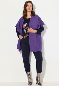 Lila stickad kofta med öppen framsida, ihop med en mörk mönstrad topp och mörka byxor. Modellen bär metalliska ankelstövlar.