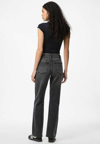 Black high-waisted jeans with a straight leg, featuring two back pockets and a subtle worn texture, paired with a fitted black top.