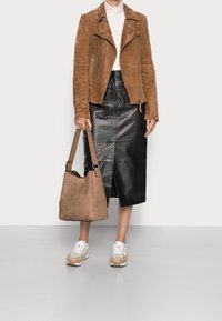 Giacca biker in camoscio marrone, dolcevita bianca, gonna midi in pelle nera con spacco frontale, borsa in camoscio beige e sneakers beige/bianche.