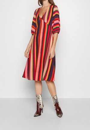 Femme portant une robe midi colorée à rayures verticales avec un col en V et des manches bouffantes, associée à des bottines pointues en cuir de serpent.