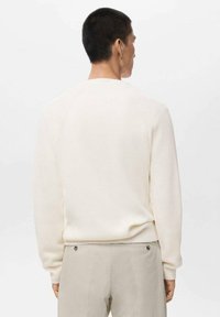 Jersey color crema con textura acanalada, cuello redondo y mangas largas de tipo raglán, combinado con pantalones beige.