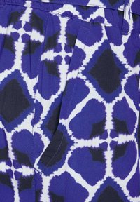 Tessuto blu e bianco con motivi astratti; presenta una tasca con dettagli di cucitura visibili. Il materiale appare liscio e leggero.