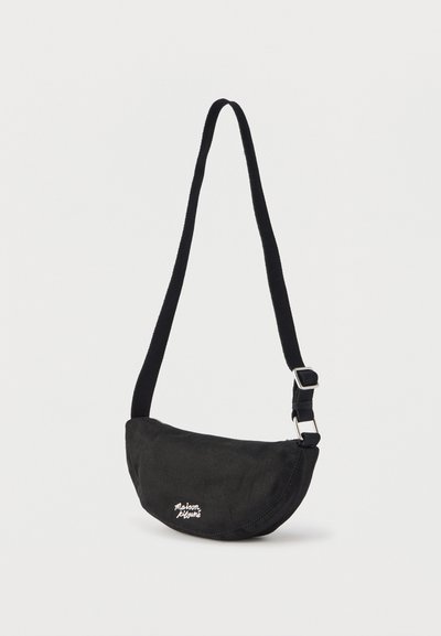 Sac bandoulière noir en forme de croissant avec une sangle ajustable et le logo blanc "Maison Kitsuné" sur le devant.