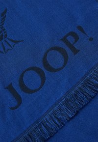 Blå tørklæde med frynser, vævet tekstur og fed sort skrift med brandnavnet "JOOP!" samt et grafisk element.