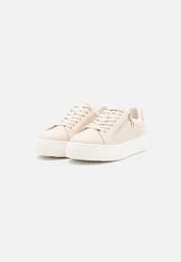 Sneaker beige con un pannello laterale testurizzato, suola piatta bianca e cerniera accentuata. Presenta chiusura con lacci e un sottile dettaglio del marchio.