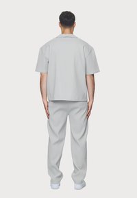 Ljusgrå outfit med kortärmad skjorta och löst sittande byxor i en texturerad tyg. Enkelt mönster, minimala detaljer och avslappnad stil.