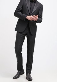 Musta frakki, jossa on satiinikaulukset, hyvin istuva takki ja litteät housut. Yhdistettynä teksturoituun mustaan solmioon ja kiillotettuihin mustiin kenkiin.