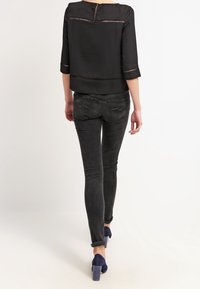 Blusa nera corta con dettagli a taglio, abbinata a jeans scuri slim-fit e tacchi blu navy. Cerniera visibile sulla schiena e dettagli delle cuciture.