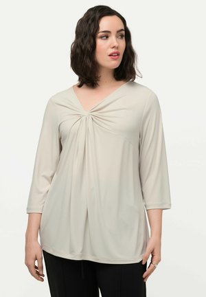Top color beige chiaro a maniche tre quarti con scollatura a V e dettaglio torcigliato sul davanti. Tessuto morbido, vestibilità rilassata e scollatura a girocollo.