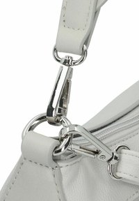 Detalle de un bolso de piel blanco que presenta un cierre metálico plateado y un enganche para la correa, mostrando un diseño elegante y una superficie texturizada.