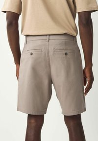 Helle graue Herren-Shorts aus Baumwollmischung, mit Gesäßtaschen und Knopfverschluss sowie geradem Schnitt. Glatte Textur, knielang.