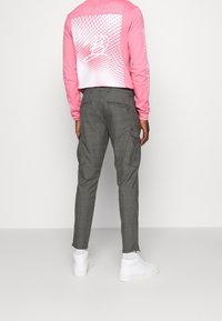 Světle růžová košile s dlouhým rukávem a grafickým potiskem na zadní straně, doplněná o šedé kalhoty na míru se bočními kapsami a bílé tenisky.