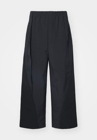 Czarne spodnie o szerokich nogawkach z elastycznym pasem, bocznymi kieszeniami na zamek i skośnymi szwami dla dodatkowej struktury. Wykonane z gładkiego, lekkiego materiału.