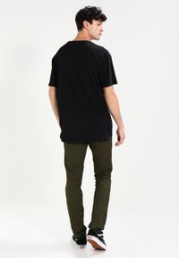Zwarte katoenen T-shirt met een losse pasvorm, gecombineerd met olijfgroene broek. Sneakers hebben een zwarte stof met witte en rode accenten.