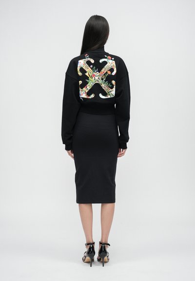 Schwarzer, kurzgeschnittener Sweatshirt mit buntem Blumenmuster auf dem Rücken, kombiniert mit einem schwarzen, figurbetonten Midikleid und schwarzen High-Heel-Sandalen.